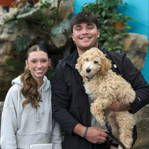 Two people with a curly-coated puppy